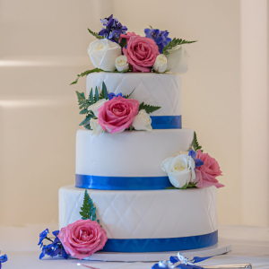 Beautiful wedding cake with pink and white rose decor and blue ribbon